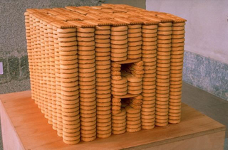 We are moving, Paola Pivi, Biscotti, 1996, biscotti, cm. 35 x 40 x 40. Composizione di migliaia di biscotti a formare una architettura essenziale, grande tanto quanto è possibile realizzare una struttura impilando dei biscotti.