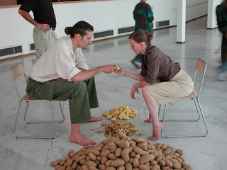 As soon as possible. Performance loop. The Class of Marina Abramovic - Braunschweig School of Art, Lotte Lindner and Till Steinbrenne, "Family II".

Lotte Lindner and Till Steinbrenner´s work is characterised by their craftsmanship background. Both are sculptors as well as performers. In their performances work and its products play a prominent role. This not only means material but as well immaterial products as sound for example. These "products" are produced by hands and bodies. In "Family II" the artists peal a huge pile of potatoes together: one holds the knife, the other the potato. This means the top of collaboration. It asumes great trust and a great sensibility for the other. The potato stands for food in general and it gives the picture back the simplicity of a Breughel genre painting.

Lotte Lindner and Till Steinbrenner´s collaboration work started in early2002 when both met in the class of Marina Abramovic. Lindner and Steinbrenner live and work in Hannover, Germany.