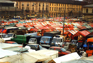 Vito Acconci. Arte, architettura e design verso lo spazio pubblico - Un confronto con la situazione della Public Art in Italia nel lavoro di 60 artisti italiani. Conferenza di Vito Acconci 14 aprile, ADRIANA TORREGROSSA,  ART. 2 , PIAZZA DEL MERCATO DI PORTA PALAZZO, TORINO, 1999

Per tre anni ho vissuto e lavorato a Casablanca e quest'esperienza è diventata anche il soggetto del mio lavoro. Invitata dal coordinamento a.titolo a realizzare un progetto per Torino, ho ideato Art. 2. Citando l'articolo 2 della Costituzione della Repubblica Italiana - elemento che evidenzia il carattere laico dell'operazione - ho seguito le fasi che hanno portato a trasmettere pubblicamente (secondo la tradizione islamica), sulla piazza del mercato di Porta Palazzo a Torino al tramonto del 17 gennaio 1999, la preghiera della riconciliazione che segna la fine del Ramadan (il mese di digiuno islamico). L'azione ha utilizzato gli strumenti del dialogo e della collaborazione con le persone. In tutte le fasi del progetto, una trattativa che ha coinvolto la sfera religiosa (la Comunità islamica di Torino), politica (l'Assessorato alla Promozione Internazionale della Città di Torino) e pubblica (The Gate, un progetto con finanziamenti della Comunità Europea per la riqualificazione del quartiere), mi sono assunta il ruolo di mediatore per portare a termine una contrattazione che si è svolta da dicembre 1998 a gennaio 1999 attraverso incontri, telefonate, fax e richieste di permesso.
Come "sito" specifico è stata individuata la piazza di Porta Palazzo, simbolo dell'immigrazione a Torino e luogo nel quale numerosi musulmani vivono e lavorano. Il progetto dunque si è svolto in un'area urbana oggi attraversata da presenze che ne modificano strutturalmente la fisionomia. L'azione pubblica è nata anche dalla necessità di ripensare la funzione dell'arte. Un progetto che si allontana volutamente dall'autoreferenzialità dell'ambiente artistico per definire un nuovo rapporto con il contesto sociale e garantendo alla fase di transizione culturale della quale siamo testimoni non una risposta univoca, ma un ampio spettro di problematiche con le quali iniziare inediti percorsi.
Il Ramadan è un momento importante per i fedeli, vissuto nella realtà Occidentale in forma silenziosa e poco visibile. La sua "amplificazione" ha voluto essere un invito a riconoscerne l'esistenza. La scelta di amplificare un momento religioso è un segnale simbolico, semplice nella forma, per evidenziare le distanze e i conflitti tra le culture. Il Ramadan che ritma il passare delle giornate, l'alimentazione e la sessualità, diventa il terreno nel quale si consumano le differenze. Tutto, la vita quotidiana come la politica, passa attraverso questo tramite ed è proprio questo aspetto che mi ha portato, pur conscia delle difficoltà e delle possibili critiche, a orientare la mia operazione in questo e non in altri ambiti culturali.
La problematicità è dunque uno degli elementi strutturali di questa operazione.
Quando domenica 17 gennaio ho dato il via alla diffusione della preghiera concludendo il mio progetto, sulla piazza erano presenti un centinaio di musulmani che hanno ascoltato la registrazione e al termine del rito hanno spontaneamente pregato in un luogo pubblico per la prima volta in Italia. La successione dei tempi ha modificato, anche se di pochi minuti, un rito religioso antico. Inoltre sulla piazza si è radunato anche un piccolo gruppo di donne. Questi dettagli apparentemente irrilevanti ai nostri occhi evidenziano come la convivenza sulla stessa scena di culture e religioni differenti modifichi necessariamente anche una dimensione che a noi pare inflessibile.